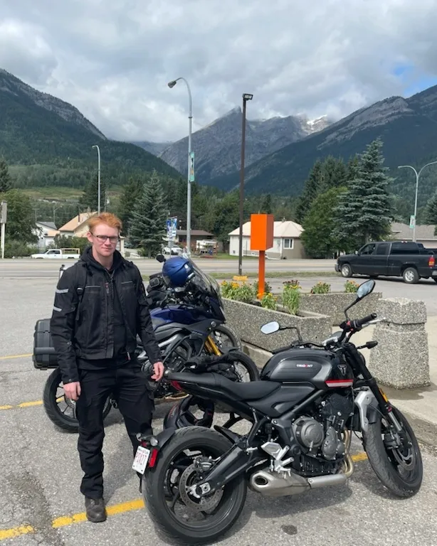 Gavin standing beside his motorcycle in the mountains
